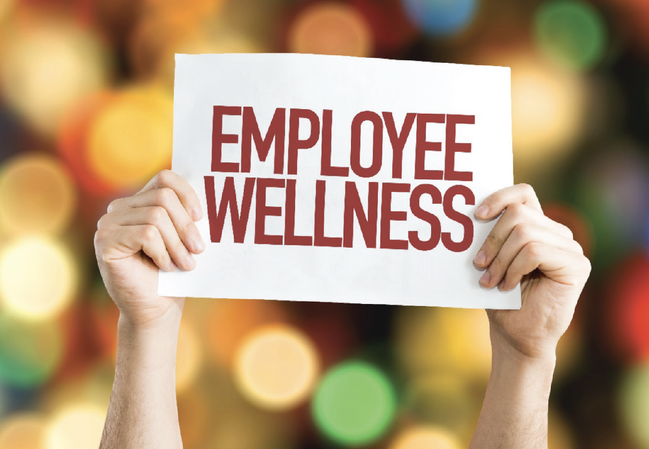  A photo of a person holding a sign that says 'Employee Wellness' in front of a blurred background of colorful lights.